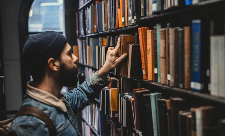 Person choosing a book from a library shelf, representing choosing A Level subjects