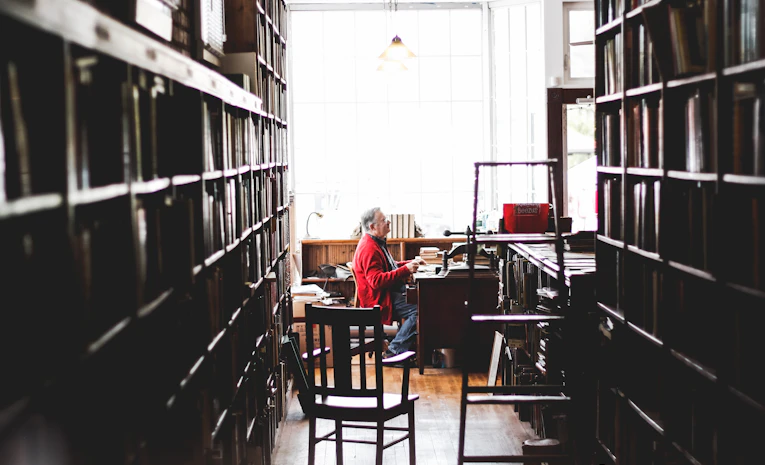 Person writing notes at a desk surrounded by books, representing dissertation writing