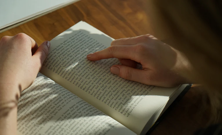 Student reading a book at a wooden table, representing dyslexia support for students