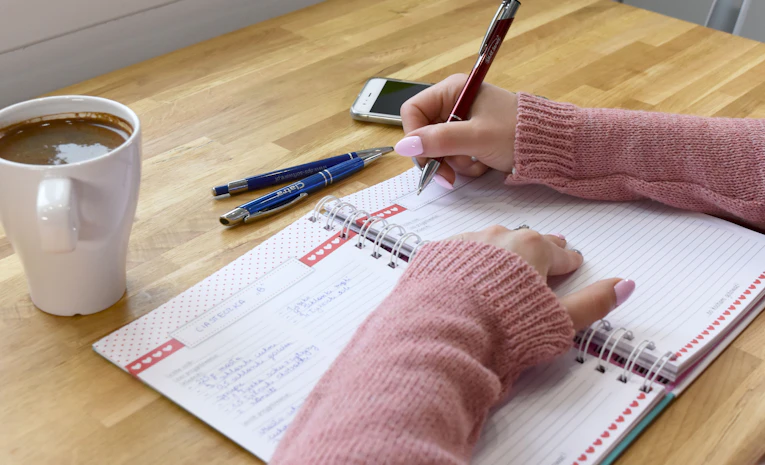 Person writing a study plan in a notebook, representing a GCSE revision timetable