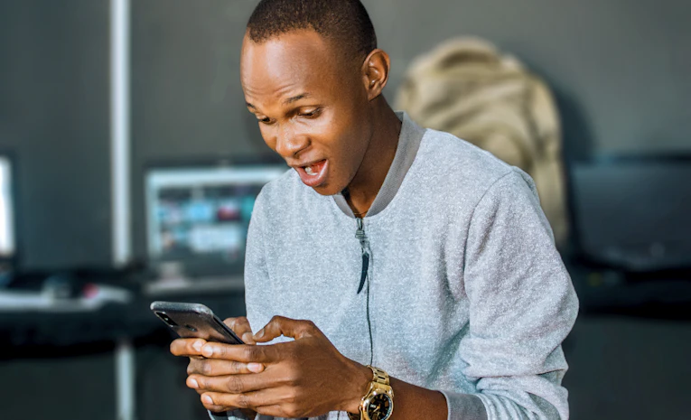 Young man smiling while looking at his phone, representing UCAS Adjustment and exam results